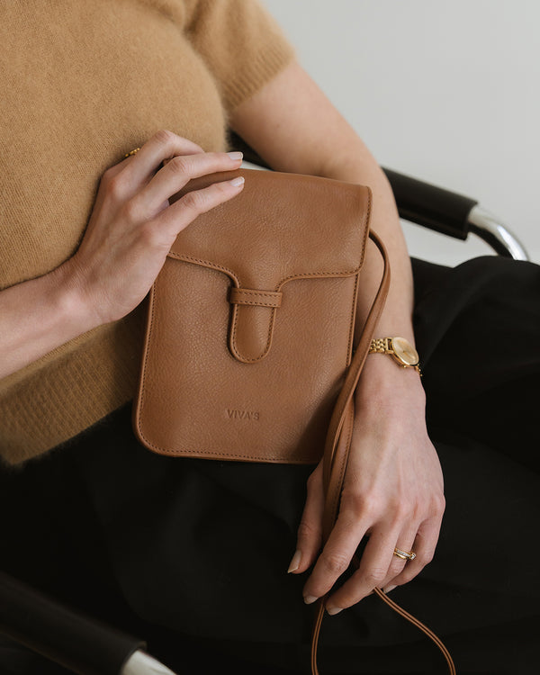 Person holding a brown leather bag with a neutral background