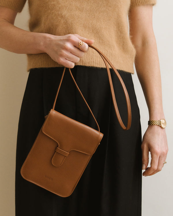 Person holding a brown leather handbag with a neutral background