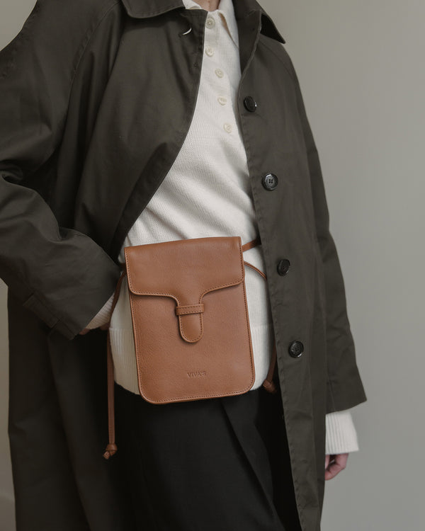 Person wearing a brown leather bag over a plain background
