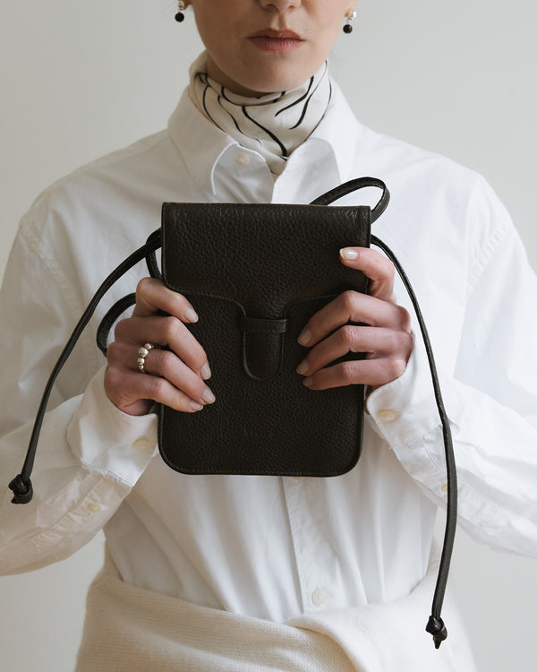 Person holding a black leather bag against a neutral background