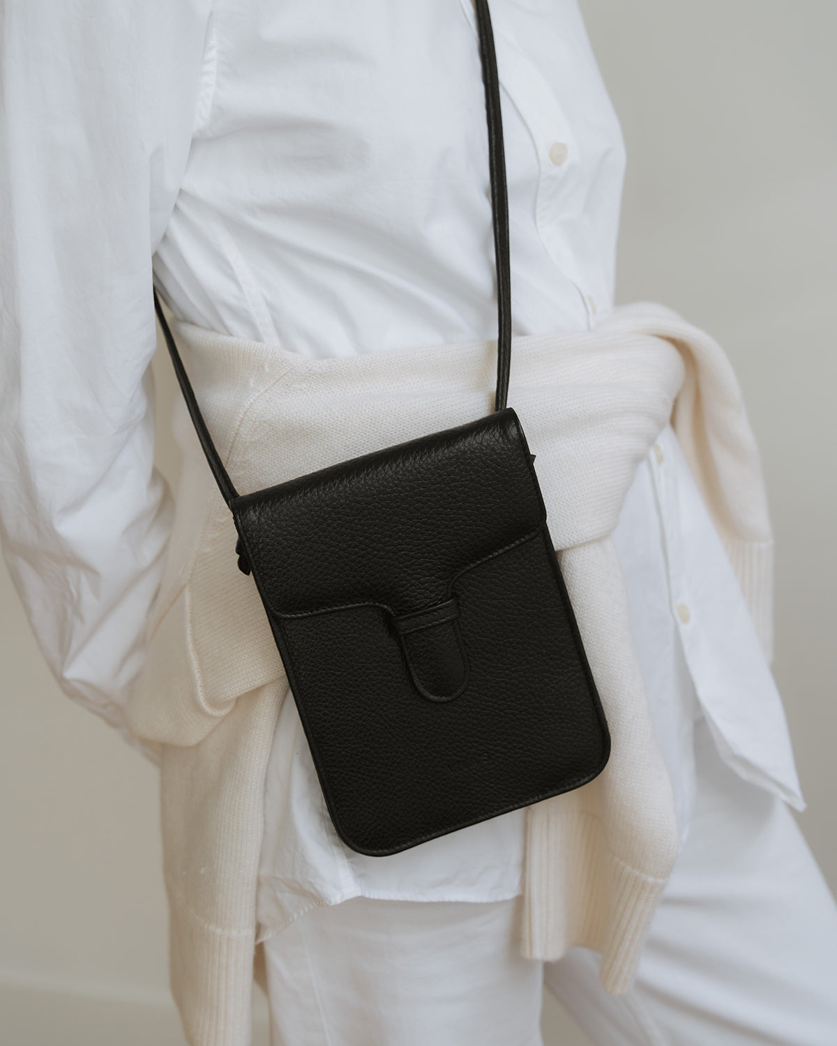 Black crossbody bag worn by a person in a white shirt and beige sweater.