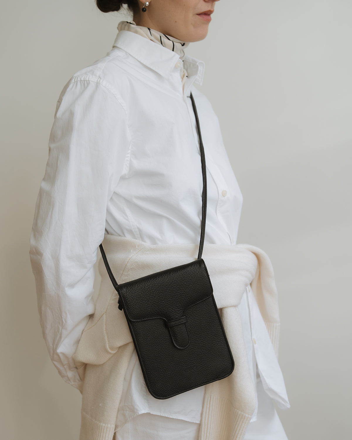 Person wearing a white outfit with a black crossbody bag on a plain background