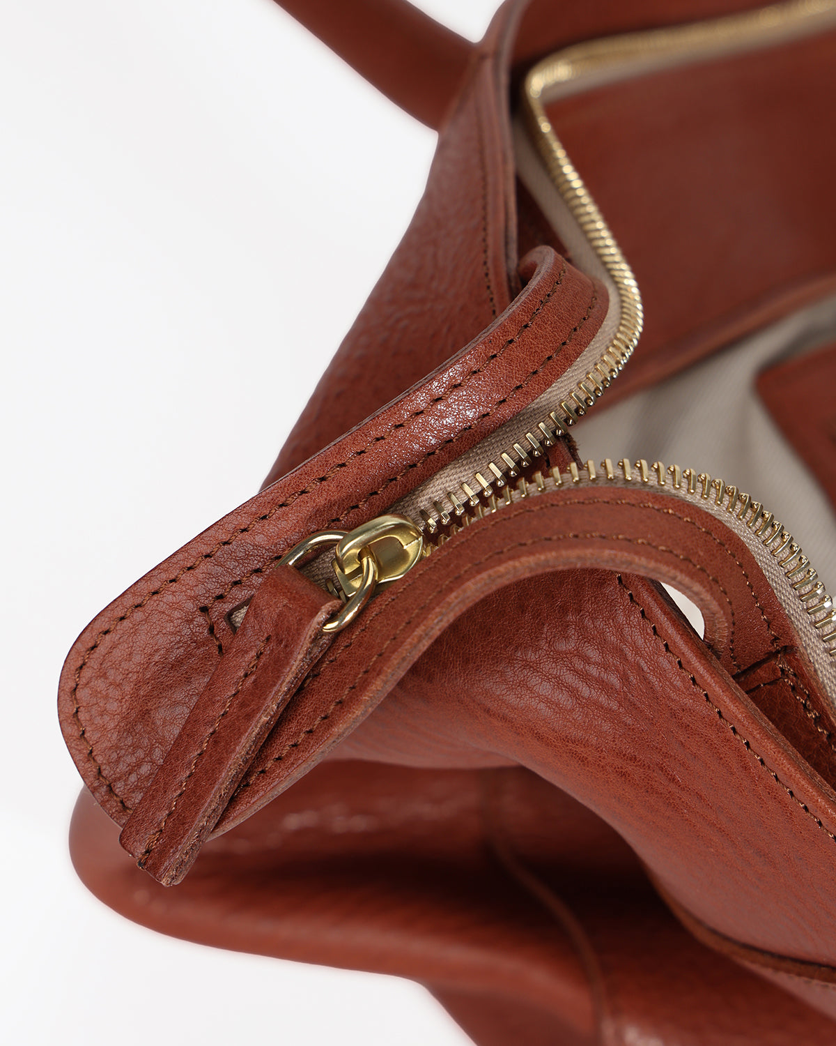Close-up of a brown leather handbag with a gold zipper on a white background