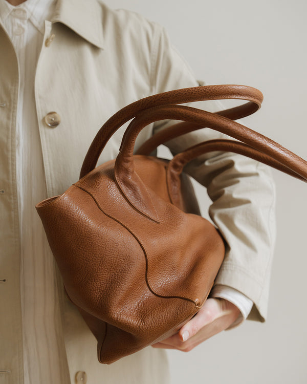Brown leather handbag held by a person wearing a beige coat.
