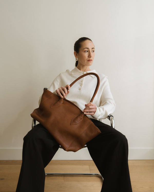 Person holding a brown leather bag in a minimalistic setting