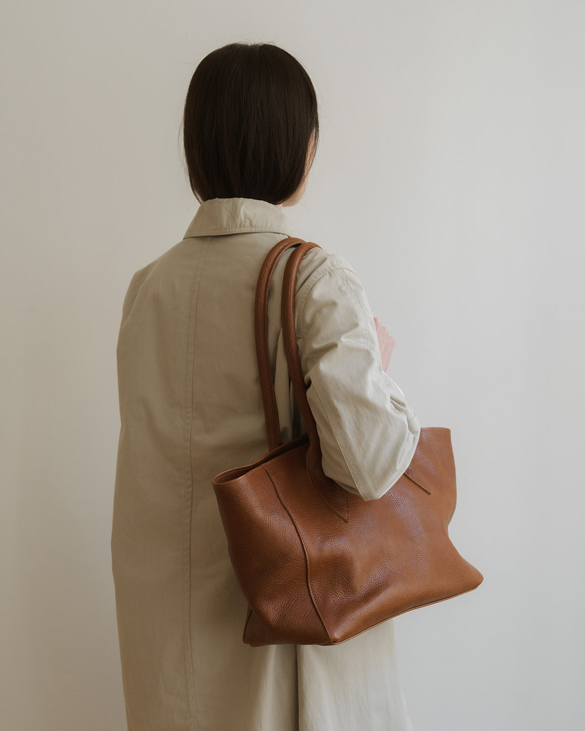 Person holding a brown leather tote bag against a plain background