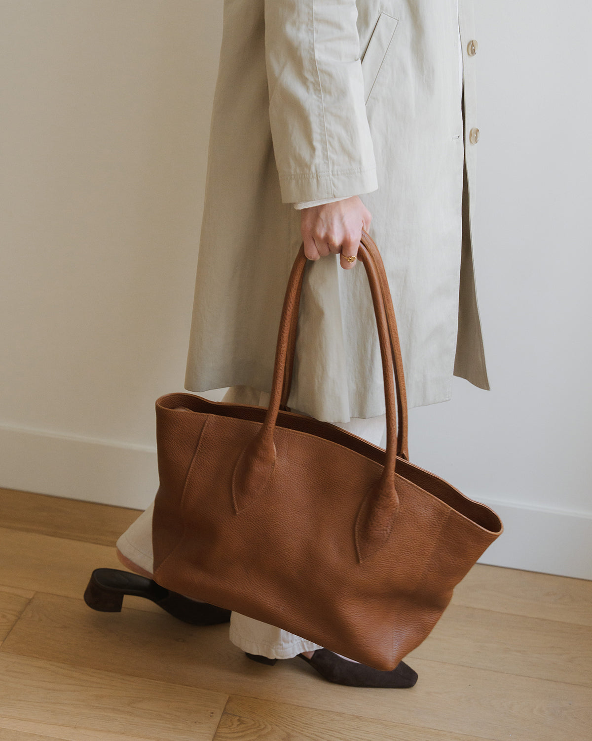 Person holding a brown leather tote bag in a minimalistic setting